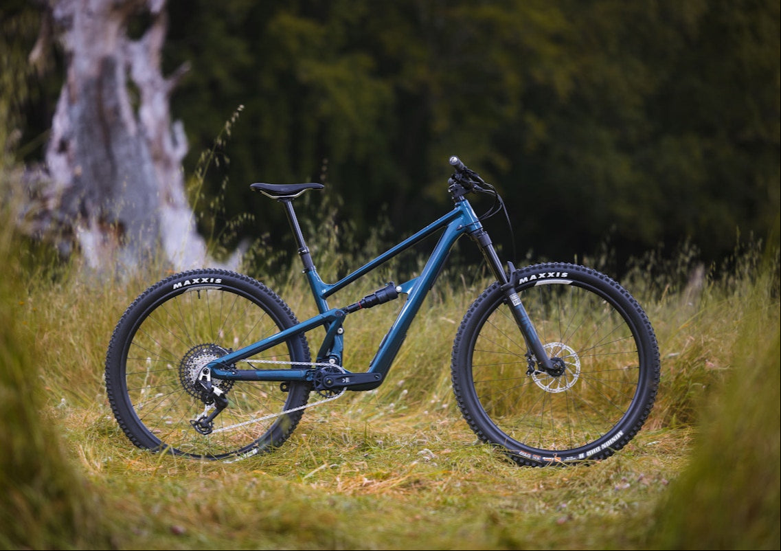 Blue mountain bike on a grassy trail with trees in the background